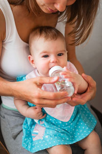 Mother helps her daughter to drink water. child learns to hold a bottle.