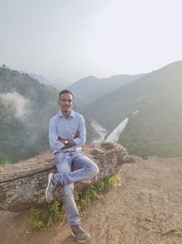 Portrait of young man standing on mountain against sky