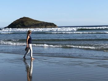 Rear view of woman walking at beach against clear sky