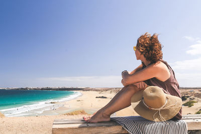 Side view of woman sitting at beach against sky