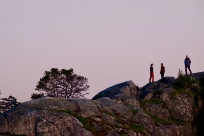 Low angle view of people standing on rock against clear sky