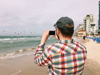 Rear view of man photographing at beach against sky