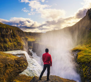 Rear view of man standing by waterfall against sky