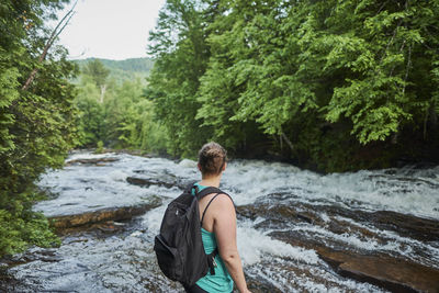 Rear view of man in river stream amidst trees in forest