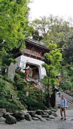 People on rock by building against trees