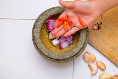 Cropped hand of woman putting red chili pepper in mortar and pestle