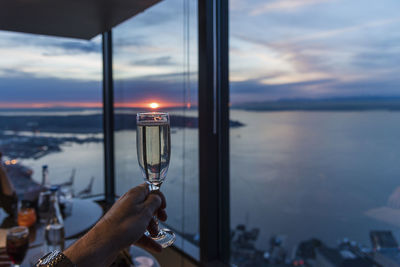 Cropped hand holding champagne flute in restaurant by sea