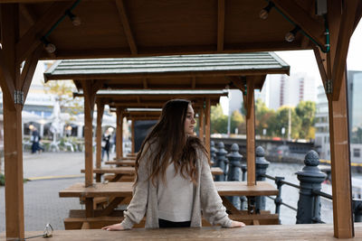 Young woman looking away while standing by table in city