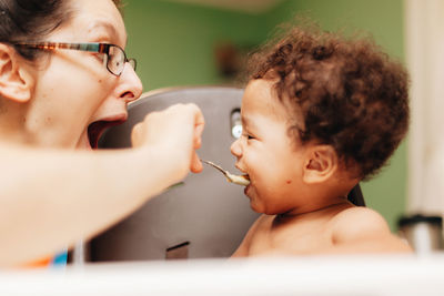 Laughing mother feeding son at home