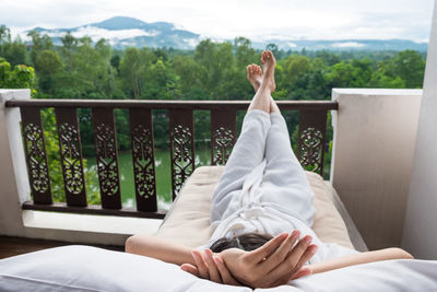 Low section of woman sitting on railing by balcony against sky