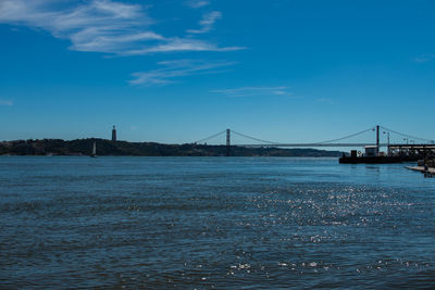 Distant view of april 25th bridge over tagus river against blue sky