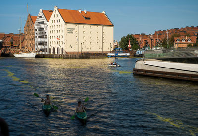 Sailboats in river by buildings in city against sky