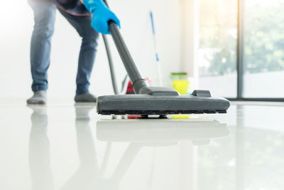 Low section of person cleaning floor with vacuum cleaner at home