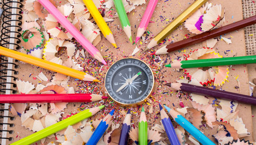 High angle view of navigational compass amidst colored pencils and shavings on diary