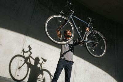 Low angle view of man picking bicycle against wall