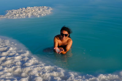 A man in a blue salt water pond exfoliating the body.