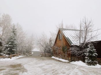 Snow covered cottage by building against clear sky