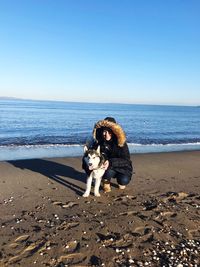 Woman with dog crouching on sand at beach against sky