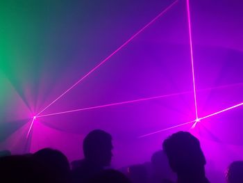 Silhouette people against light beams at nightclub