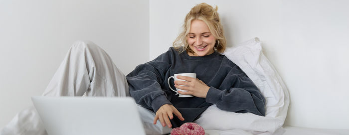 Young woman using digital tablet while sitting on bed at home