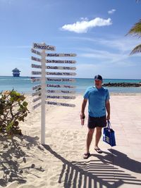 Man standing by sign board at beach against sky