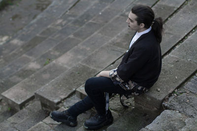 Side view of young man sitting on footpath