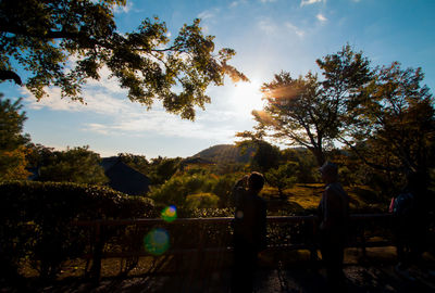 People by trees against sky during sunset