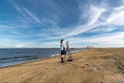Side view of teenage girl photographing at beach against sky