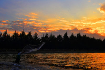 Man fishing at lake against sky during sunset