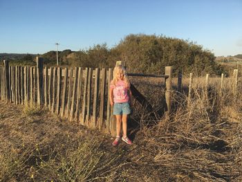 Portrait of girl standing by wooden fence at wilder ranch state park against clear sky