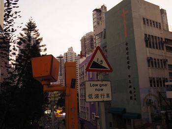 Road sign by buildings in city against sky
