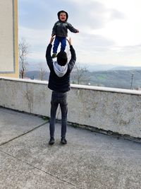 Full length portrait of man standing on railing against sky