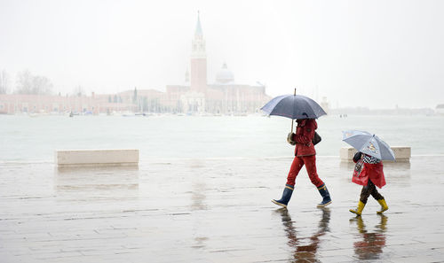 Man walking with child against grand canal by santa maria della salute during rainy season