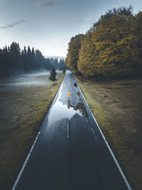 Empty wet road by trees against sky