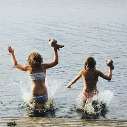 Rear view of mother and daughter holding stuffed toys while standing in lake