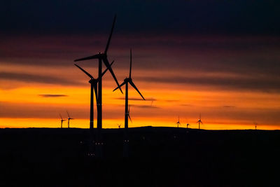 Silhouette wind turbines on land against sky during sunset