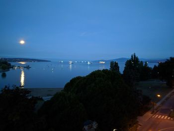 Illuminated city by sea against sky at night