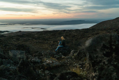 Man standing on rock against sky during sunset