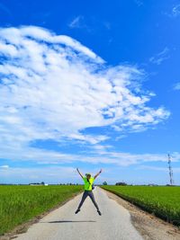 Woman walking on road amidst field against sky