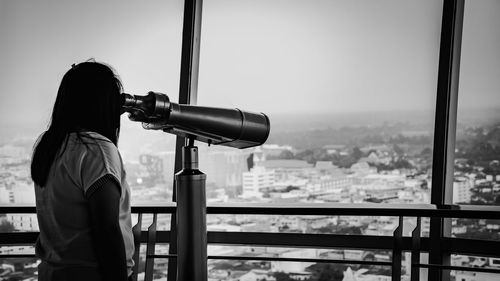 Rear view of woman looking through binoculars at cityscape
