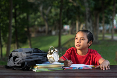 Thoughtful boy studying on table in park