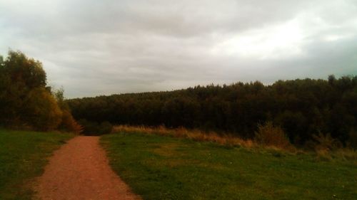 Road amidst trees on field against sky