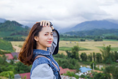 Portrait of smiling young woman standing on landscape against sky