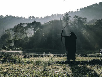 Rear view of man standing on field against trees