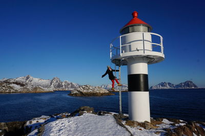 Lighthouse by sea against clear blue sky