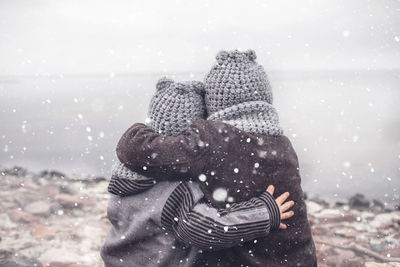 Girl in knitted grey hat hugging her frozen smaller brother