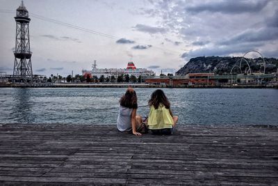 Rear view of women sitting on bridge against sky