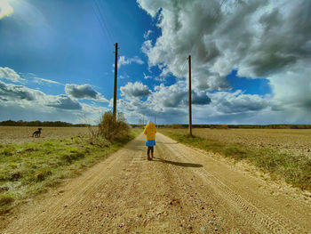 Rear view of child walking on road amidst field against sky