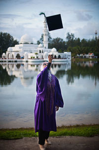 Rear view of woman standing by lake against sky