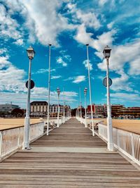 View of boardwalk on bridge against blue sky